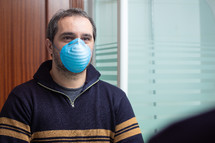 worried man with medical mask looking in the mirror