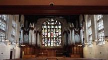 Inside a cathedral or catholic church look at stained glass windows, pews, an organ, and pipes with beautiful sunlight shining through.