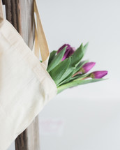 Purple tulips in a canvas bag, which is hanging on the back of a chair.