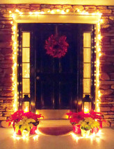 Christmas lights, wreath and poinsettia plants decorate the front door entrance to a home getting ready for family and friends over the holidays to celebrate Christmas time and make a house feel like a home. 