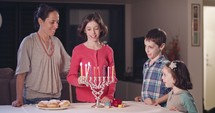 Kids and their mother lighting Hanukkah candles.