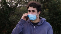 a young man wearing a face mask talking on a cellphone outdoors 