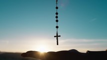 Silhouette of Hand of Man praying at sky with rosary