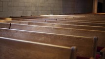 Slow-motion dramatic shot of empty wooden church pews with a brick wall in the background and light shining in.