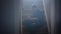 a man sitting on steps reading a Bible and praying to God 