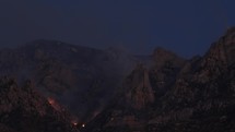 A wildfire and smoke in rugged mountains at night