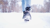 Close-up of female legs walking in winter snowy park. Woman walking in winter day. Black winter boots on legs. Active lifestyle at nature.