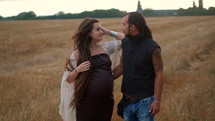 Man in a black cloth and a pregnant woman in a black long dress and dreadlocks embrace and are kept in hand, against the background of yellow grass field, nature, autumn or summer. love story