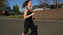 A young woman jogging down a residential street.