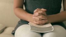 woman sitting on a white couch reading a Bible and praying 