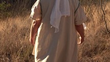 Jesus or a Bible prophet opens his arms while walking in the desert