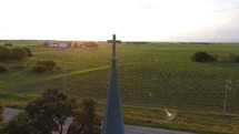 Aerial orbit of a cross on top of a church steeple in a small town
