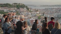 People watch the sunset with the backdrop of the 25th of April Bridge in Lisbon Portugal from atop Miradouro da Senhora do Monte