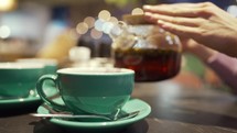 Tea Time. Person fills cup of tea in the restaurant. Close up. Woman pouring tea into a cup in coffee shop.