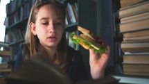 A schoolgirl girl snacks on a cheese sandwich during a class in the library. College education. Self-study in the library with books.