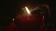 A Candle With A Flame In A Dark Room Where There Is Smoke From Other Candle's Gone Out.