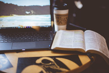 laptop computer, coffee cup, and opened Bible on a table 