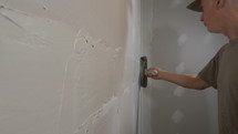 A construction workman troweling plaster while taping drywall