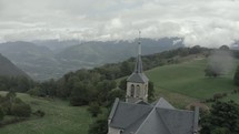 Aerial shot of beautiful gothic church with green hills and mountains in background 
