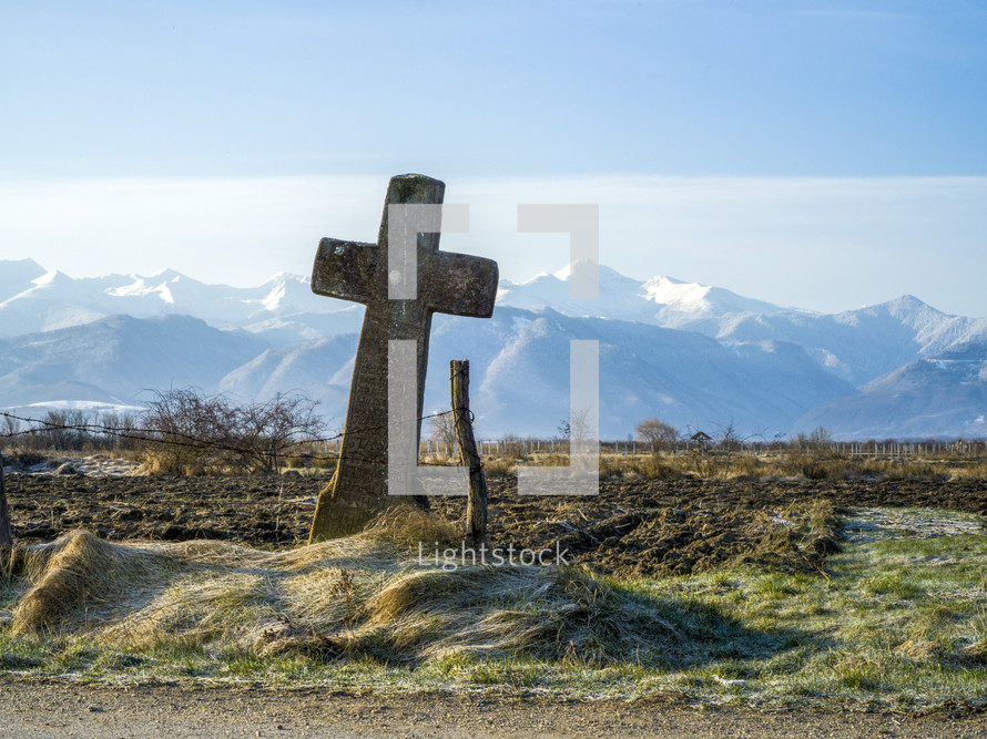 cross and fence in front of snow capped mountains 