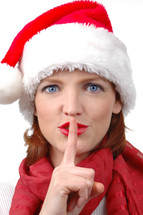 A woman in a Santa hat with her finger to her lips saying "sshhh."