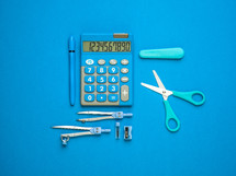 calculator, scissors, pen, compass, school supplies on blue 