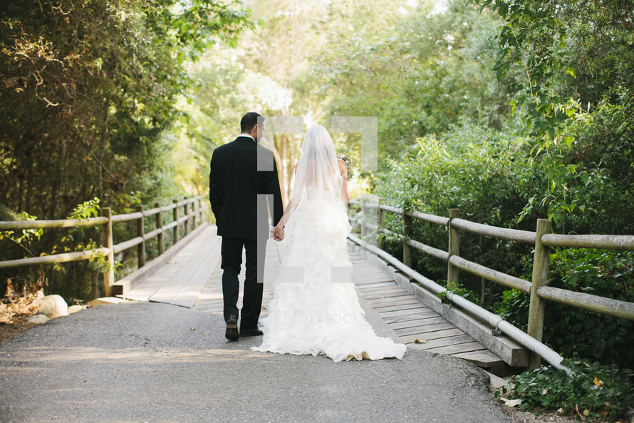 bride and groom holding hands walking across a wood bridge