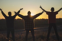 young men with hands raised at sunset 