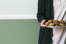 a torso of a woman holding a plate of cookies 