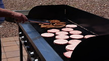A man cooking brats and burgers on a grill for a large group