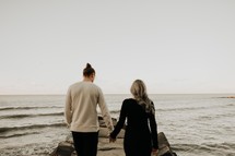 a couple walking onto a rock jetty 