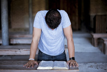 man kneeling in prayer over a Bible 