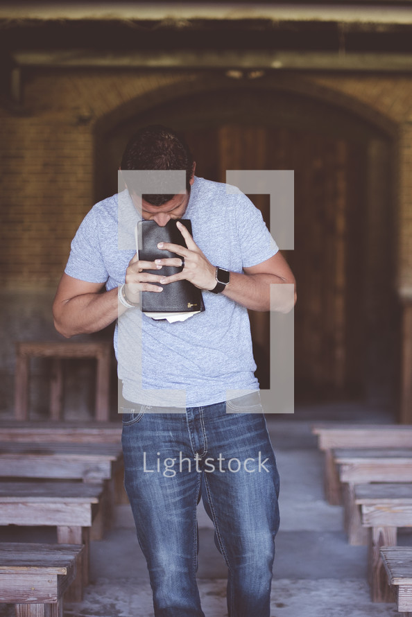 man standing in an empty church holding a Bible 