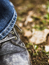 a boot and jeans standing on the ground in a forest 