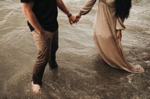 a couple holding hands standing in water 