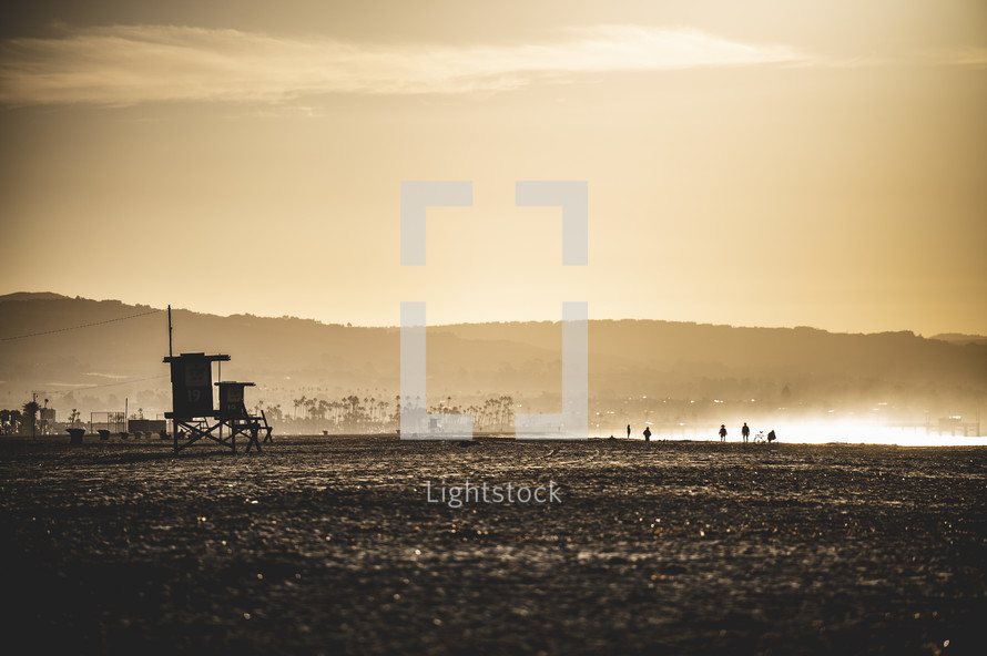 silhouettes of people walking on a  beach at sunset and Lifeguard stand 