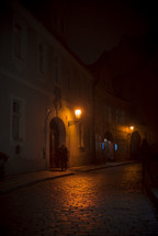 a glowing street lamp at night over a cobblestone street 