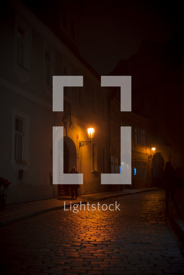 a glowing street lamp at night over a cobblestone street 