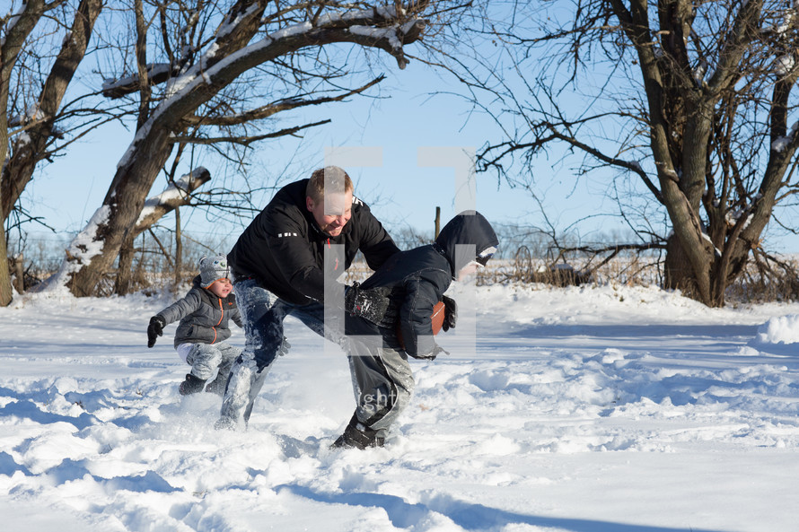 father and sons playing football in the snow 