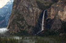 Mountain in Yosemite with waterfall and foggy trees