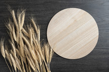Round wood tray with ears of wheat on a dark wood background