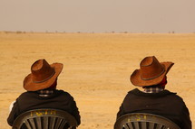 men with cowboy hats sitting in chairs in a desert 