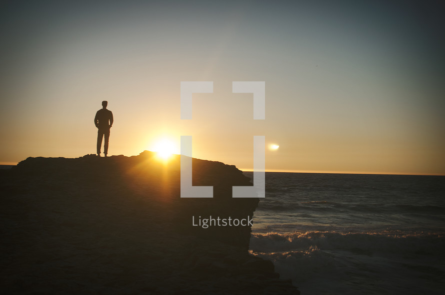 man standing on a cliff and a sunburst 