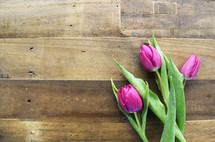 Three purple tulips laying on a wooden surface.