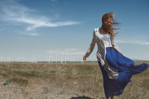 a woman in a flowing skirt standing in front of a wind farm 