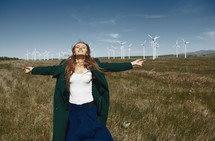 a woman with outstretched arms standing in front of a wind farm 