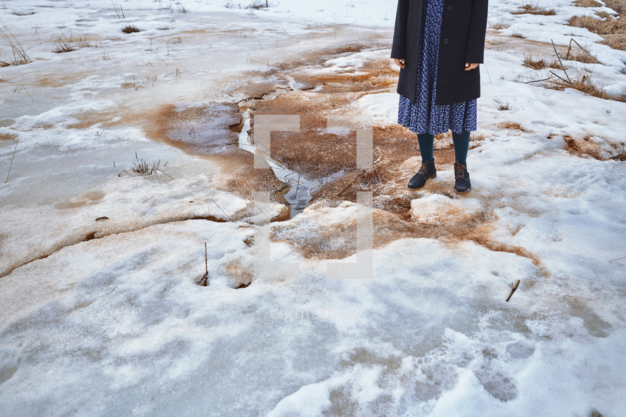 Woman standing at the puddle in winter landscape