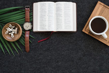 watch, Bible, coffee, tray, and palm fronds on a desk 
