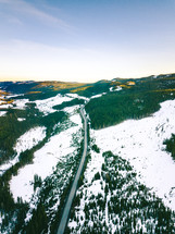 aerial view over a road through an evergreen forest in winter 