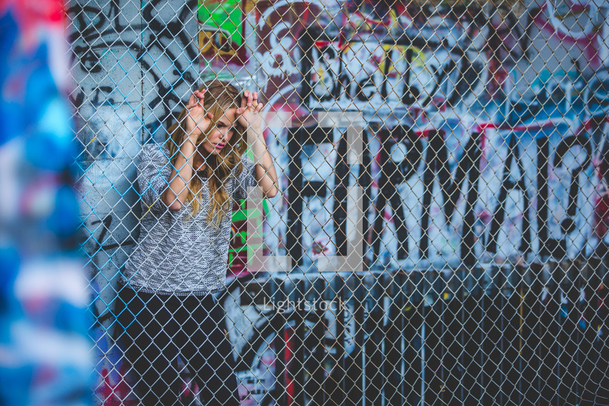a woman behind a chain link fence and graffiti 